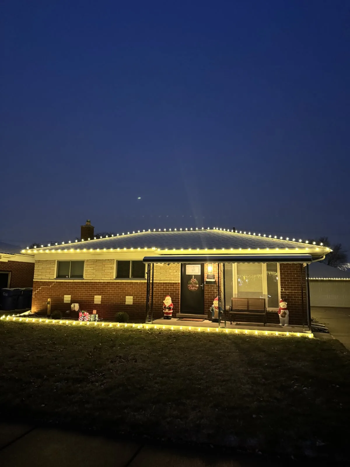 Professional Christmas light installation on a Metro Detroit ranch — roofline, gutter line and ground-level lights at dusk