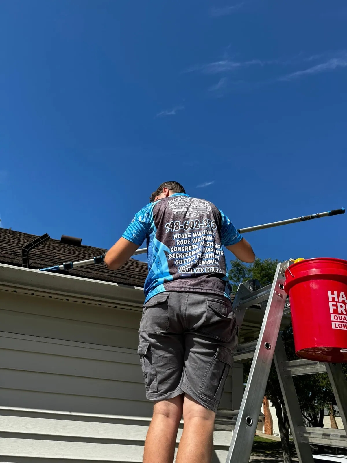 Restoration Pressure Washing technician clearing gutters from a ladder